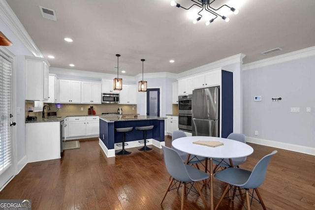 kitchen featuring appliances with stainless steel finishes, dark stone countertops, a kitchen island with sink, white cabinetry, and pendant lighting