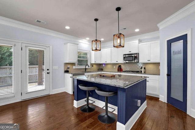 kitchen featuring a center island, decorative light fixtures, appliances with stainless steel finishes, white cabinets, and light stone countertops