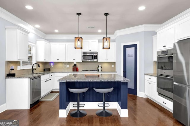 kitchen with pendant lighting, appliances with stainless steel finishes, white cabinets, a kitchen island, and light stone countertops