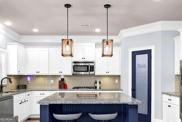 kitchen with a kitchen island, appliances with stainless steel finishes, decorative light fixtures, light stone countertops, and a sink