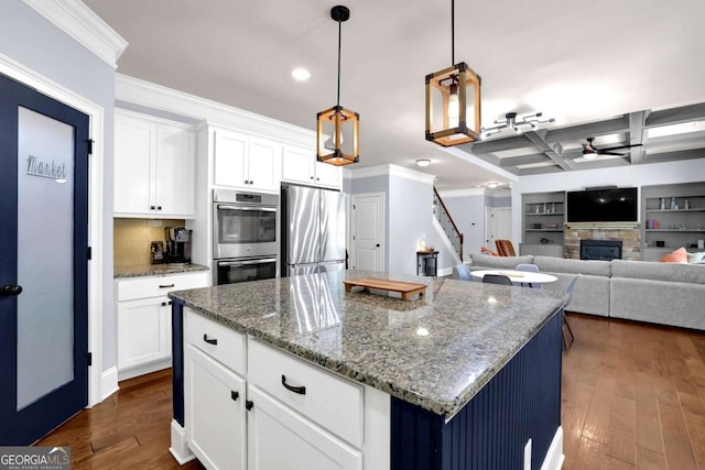 kitchen with white cabinets, a center island, stainless steel appliances, stone counters, and a fireplace