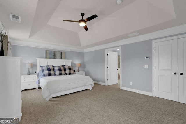 carpeted bedroom with a ceiling fan, visible vents, baseboards, a tray ceiling, and crown molding