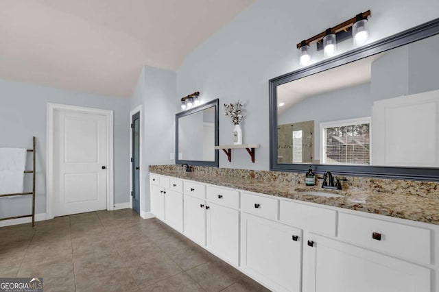 bathroom with a sink, baseboards, vaulted ceiling, tile patterned floors, and double vanity