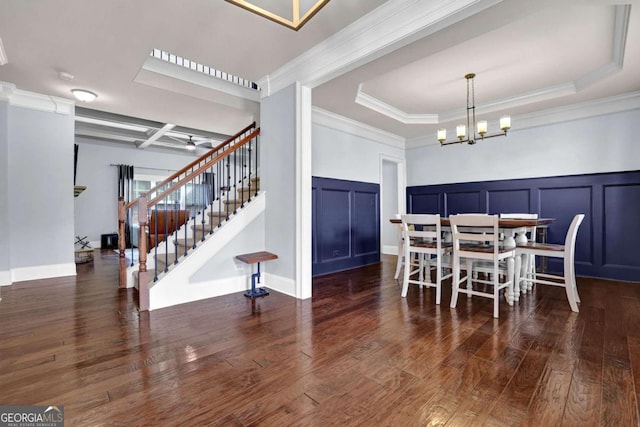 dining space featuring a decorative wall, dark wood finished floors, stairway, a raised ceiling, and an inviting chandelier