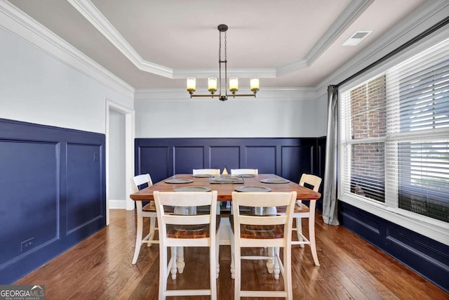 dining area with a raised ceiling, wainscoting, dark wood-style flooring, crown molding, and a notable chandelier