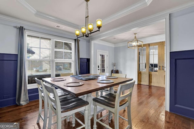 dining room with crown molding, dark wood-style flooring, a raised ceiling, and an inviting chandelier