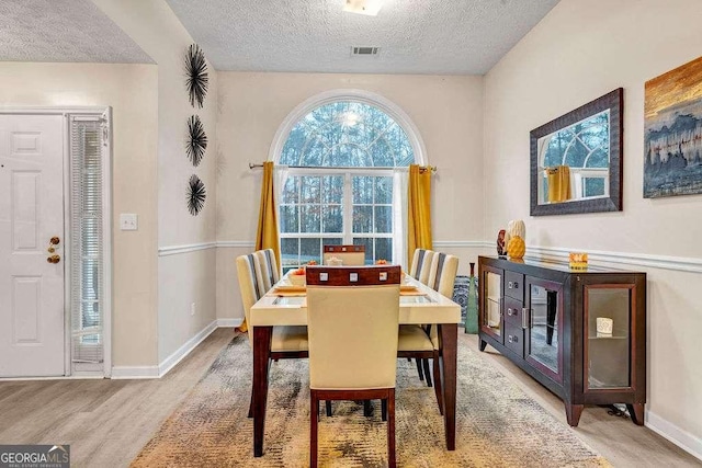 dining room featuring a textured ceiling, baseboards, visible vents, and light wood-style floors