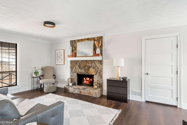 living room featuring hardwood / wood-style flooring, baseboards, visible vents, and a stone fireplace