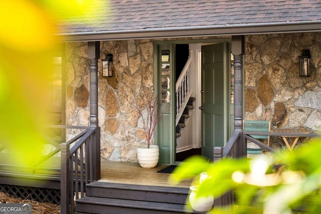 entrance to property with stone siding and a shingled roof