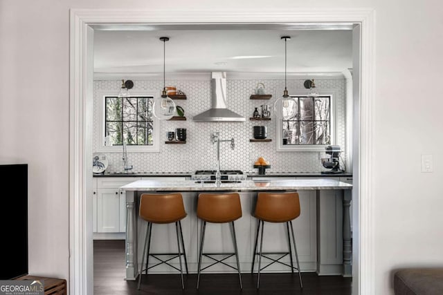 bar featuring dark wood-style floors, backsplash, pendant lighting, and wall chimney range hood