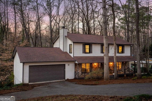 traditional-style home featuring a chimney, a shingled roof, covered porch, concrete driveway, and a garage