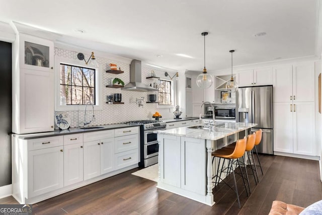 kitchen with appliances with stainless steel finishes, white cabinets, a sink, and wall chimney range hood