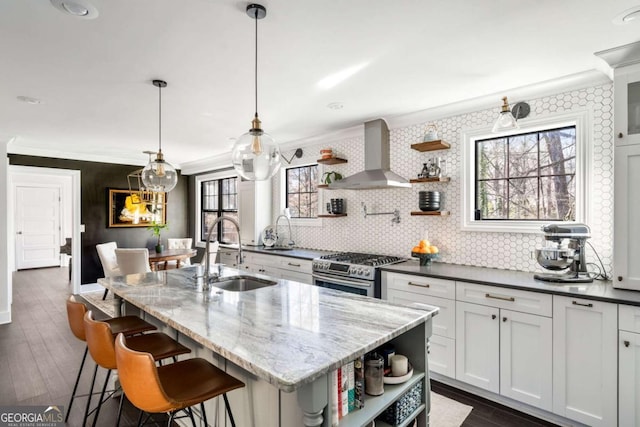 kitchen featuring dark wood-style flooring, open shelves, stainless steel range with gas stovetop, a sink, and wall chimney range hood