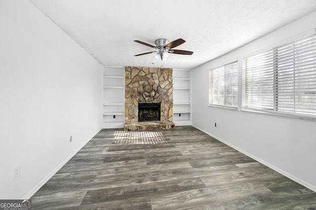 unfurnished living room with dark wood-style floors, baseboards, a textured ceiling, and a stone fireplace