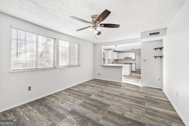 unfurnished living room featuring a textured ceiling, dark wood-type flooring, and a ceiling fan