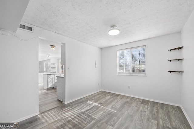 empty room with baseboards, visible vents, a textured ceiling, and light wood finished floors