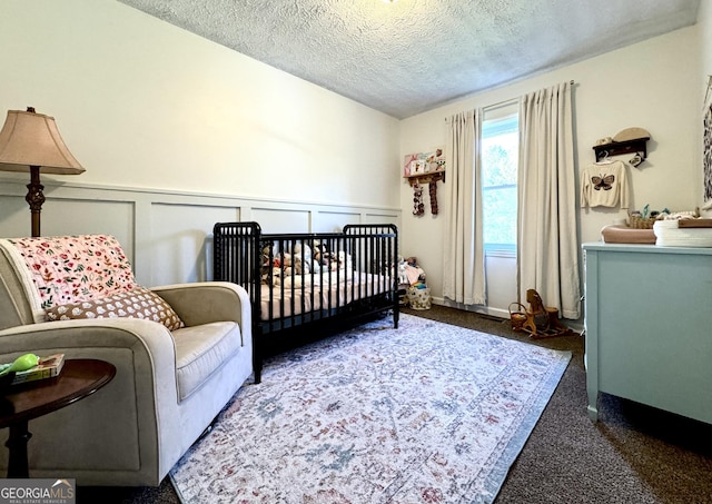 bedroom with dark carpet, a decorative wall, wainscoting, a textured ceiling, and a crib