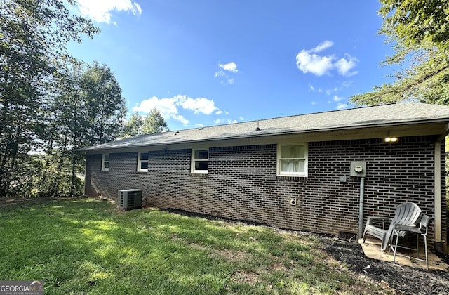 view of side of property with cooling unit, brick siding, and a yard