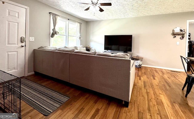 living room with a textured ceiling, ceiling fan, light wood-type flooring, and baseboards