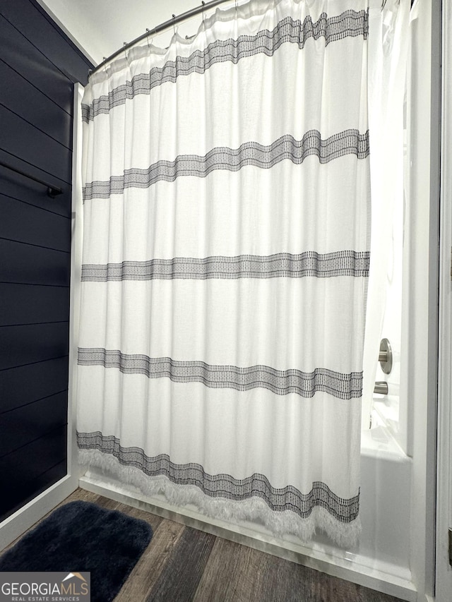 bathroom with curtained shower, wooden walls, and wood finished floors