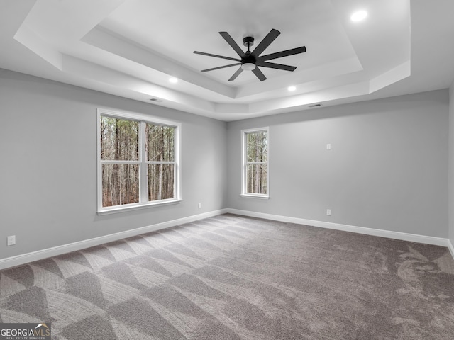 empty room featuring carpet floors, a tray ceiling, a ceiling fan, and baseboards