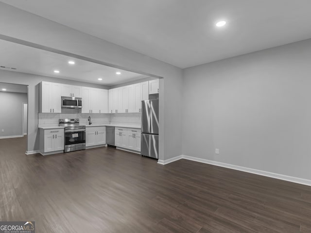 kitchen with dark wood finished floors, light countertops, backsplash, appliances with stainless steel finishes, and white cabinetry