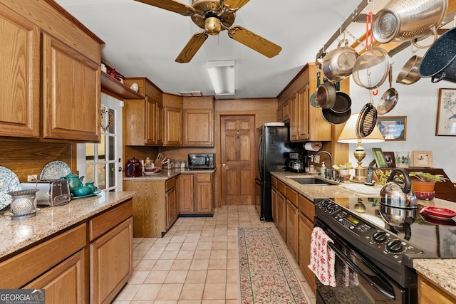 kitchen featuring light tile patterned flooring, a sink, brown cabinets, light stone countertops, and black appliances