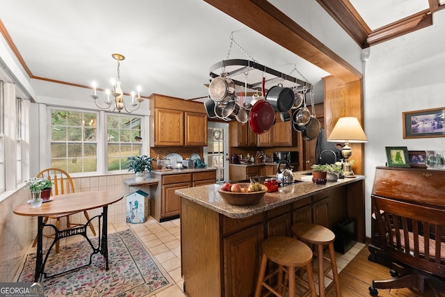 kitchen with ornamental molding, brown cabinets, a breakfast bar area, and an inviting chandelier