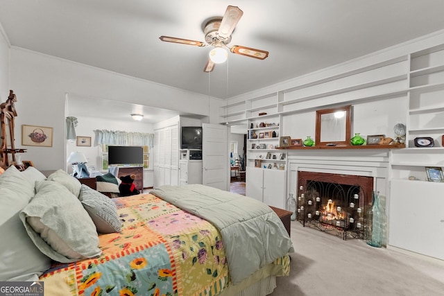 carpeted bedroom featuring a ceiling fan, crown molding, and a lit fireplace