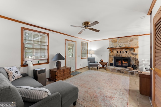 living area featuring crown molding, light tile patterned floors, a ceiling fan, a stone fireplace, and baseboards