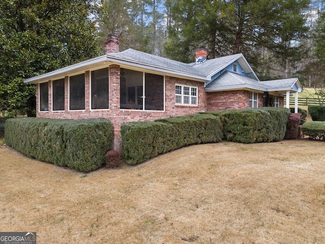 view of side of property with brick siding, a chimney, and a lawn