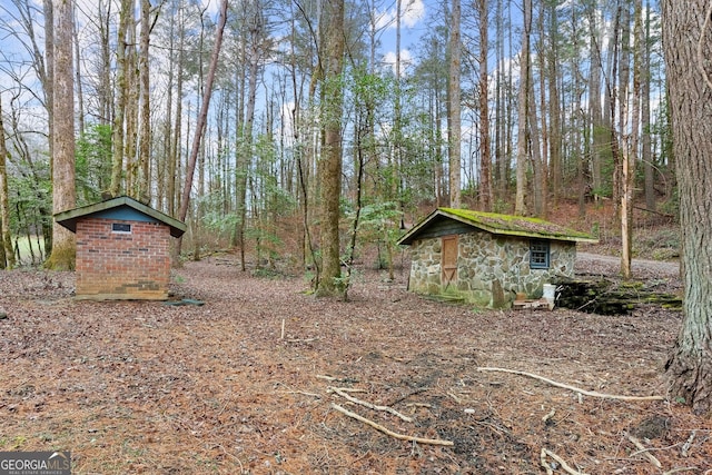 view of yard featuring a forest view, an outdoor structure, and a storage shed