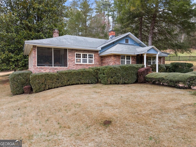 view of front facade with brick siding, a chimney, a front lawn, and fence