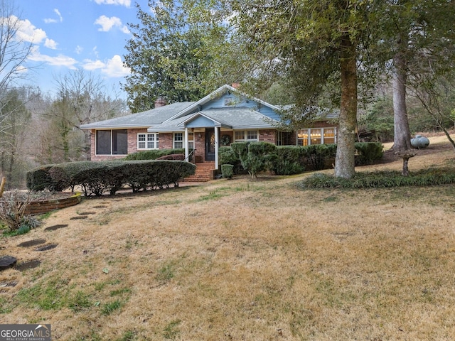 view of front of home featuring a front yard, a chimney, and brick siding