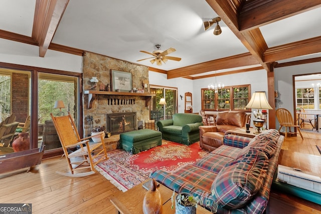 living area with a stone fireplace, ceiling fan with notable chandelier, beam ceiling, wood-type flooring, and crown molding