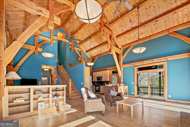 living room featuring beam ceiling, wood ceiling, ceiling fan, wood finished floors, and stairs