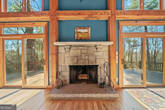 living area with a stone fireplace, wood finished floors, and a towering ceiling