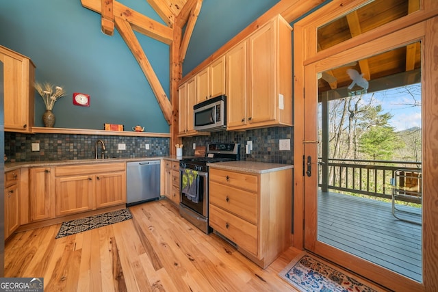 kitchen featuring light wood finished floors, backsplash, appliances with stainless steel finishes, a sink, and vaulted ceiling