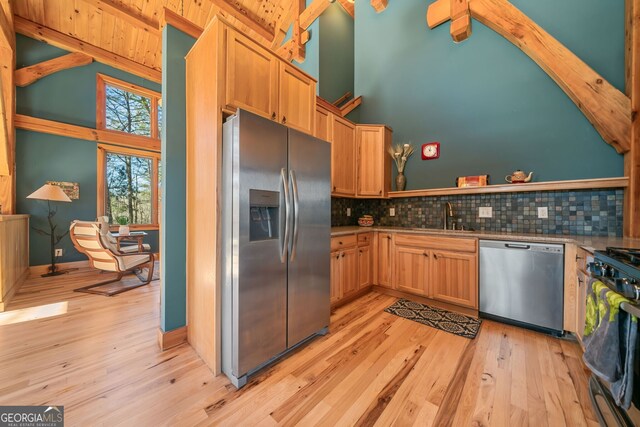 kitchen featuring light wood finished floors, stainless steel appliances, tasteful backsplash, a sink, and high vaulted ceiling