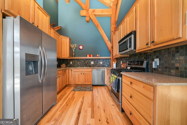 kitchen with decorative backsplash, appliances with stainless steel finishes, light countertops, light wood-style floors, and a sink