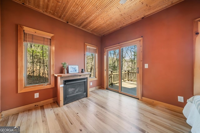 doorway to outside with wood finished floors, a glass covered fireplace, wood ceiling, and a healthy amount of sunlight