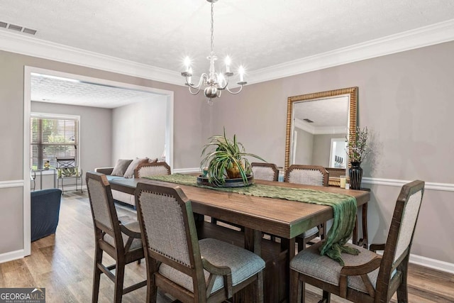 dining area featuring a notable chandelier, crown molding, visible vents, and wood finished floors
