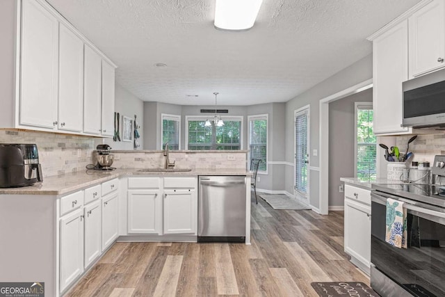 kitchen with a peninsula, appliances with stainless steel finishes, a sink, and white cabinetry