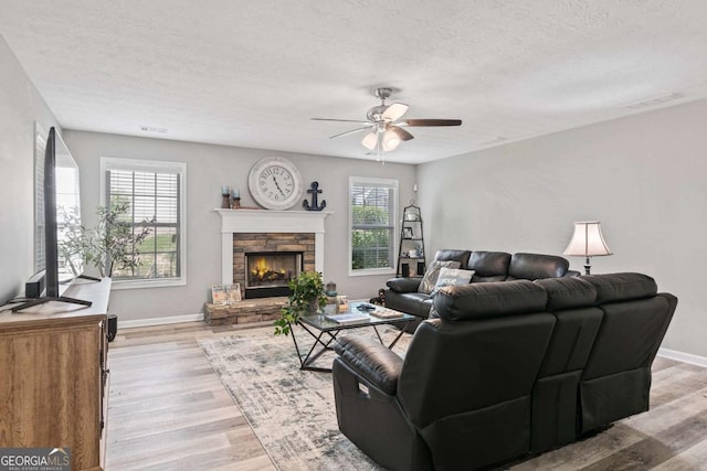 living room with light wood-style flooring, a fireplace, baseboards, and a textured ceiling