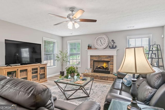 living area with visible vents, a stone fireplace, a wealth of natural light, and light wood-style floors