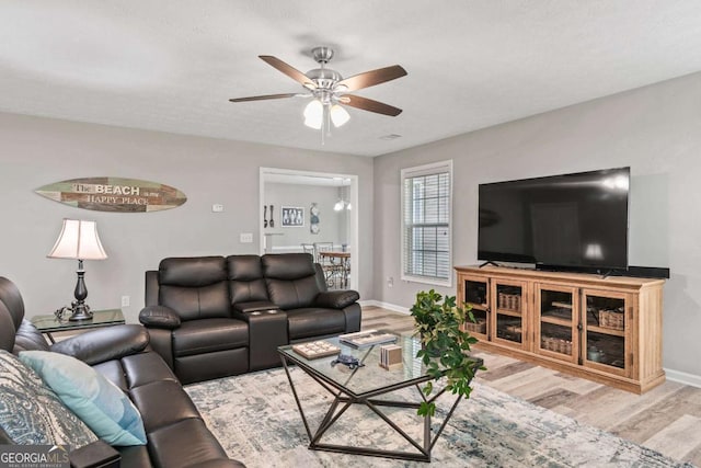 living area featuring light wood-type flooring, baseboards, and a ceiling fan