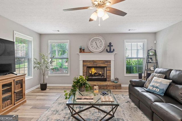 living area featuring light wood-style flooring, a fireplace, visible vents, and a healthy amount of sunlight