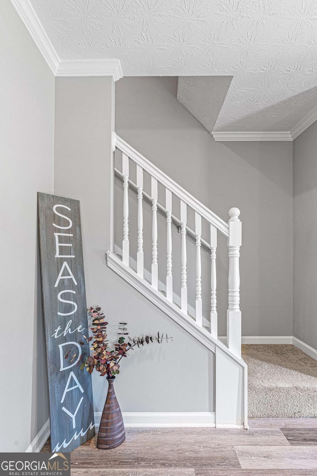 stairs with crown molding, a textured ceiling, baseboards, and wood finished floors