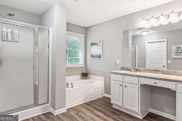 full bath featuring wood finished floors, a garden tub, a textured ceiling, vanity, and a shower stall