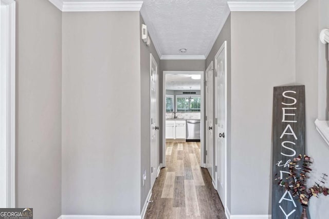 corridor with crown molding, a sink, a textured ceiling, wood finished floors, and baseboards